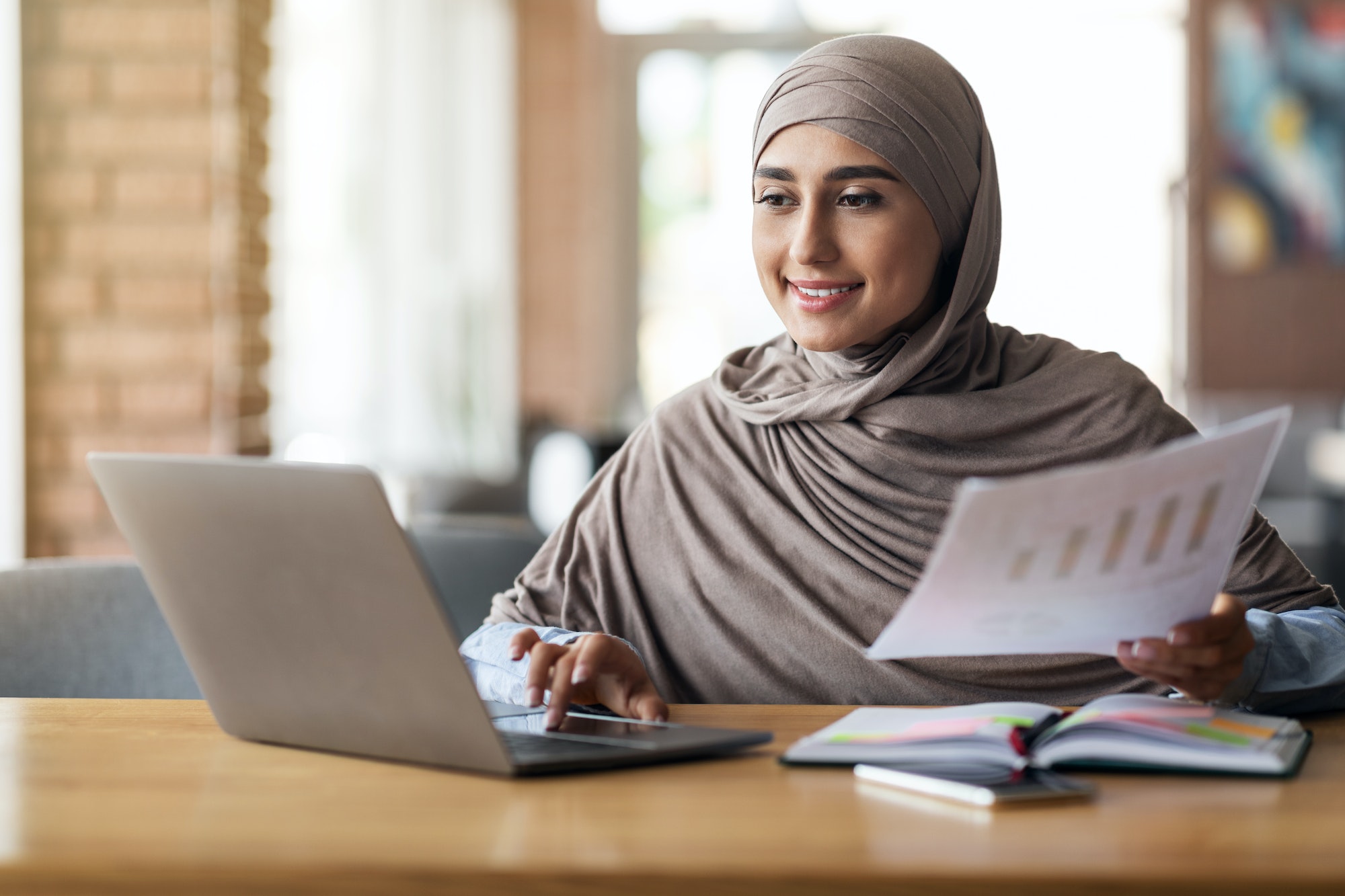 Muslim woman business analyst working on laptop at cafe